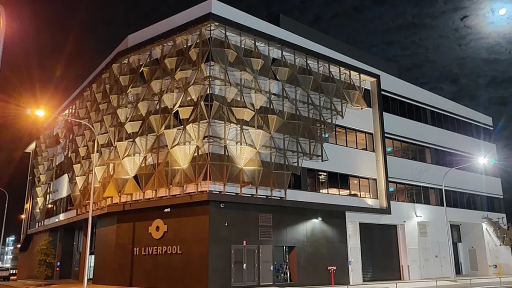 The Australian Taxation Office building in Townsville, Queensland, at night, showing its gold-lit angular facade, lit office windows and the 11 Liverpool address sign on the wall. Photographed in 2020; not from the ATO report's release.
