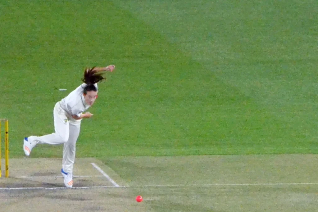 Megan Schutt in Test whites in her bowling follow-through on a floodlit pitch, the pink ball on its way down the wicket.