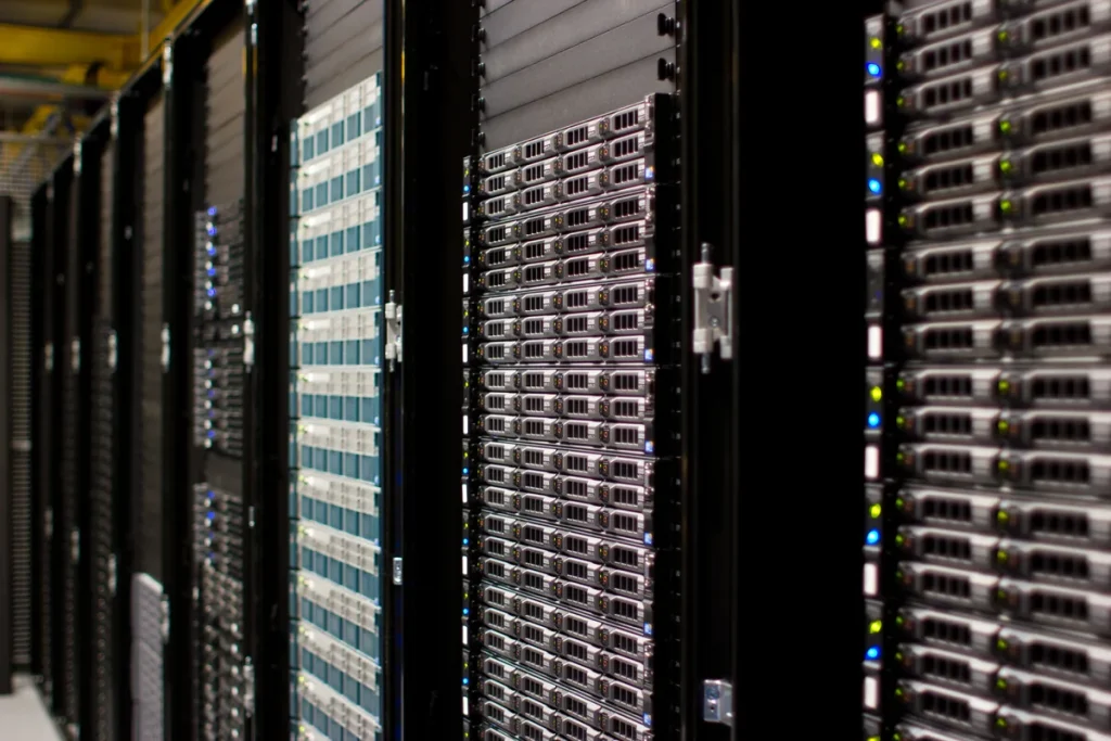 Close view of tall black server racks filled with rows of rack-mounted servers, small blue and green status lights glowing in a dim data centre aisle.