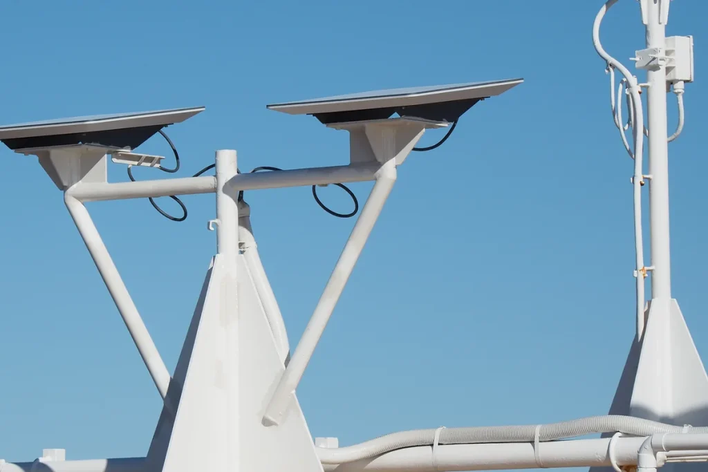 Two flat rectangular satellite internet terminals mounted on a white ship's mast against a clear blue sky, with looping black cables and white conduit.