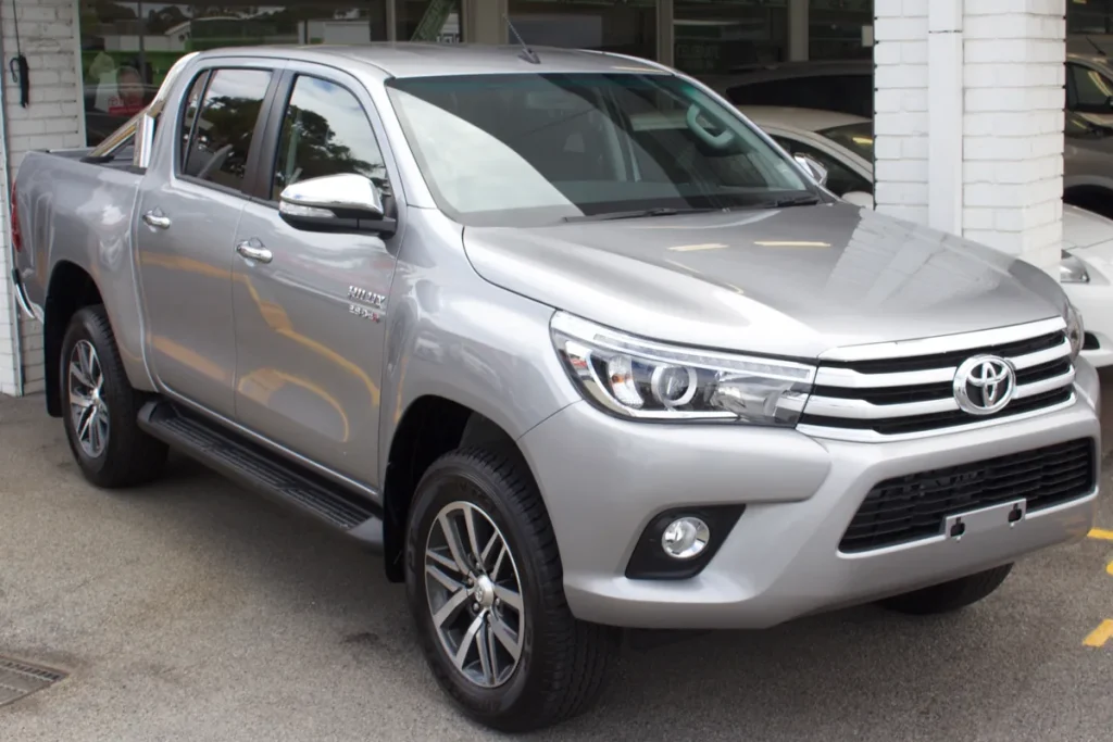 A silver Toyota HiLux SR5 dual-cab utility parked on a dealership forecourt, seen from the front right, with no number plate fitted.