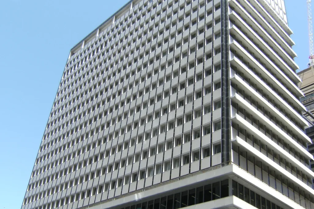 A grey modernist office tower with a grid of recessed windows rising into a clear blue sky.